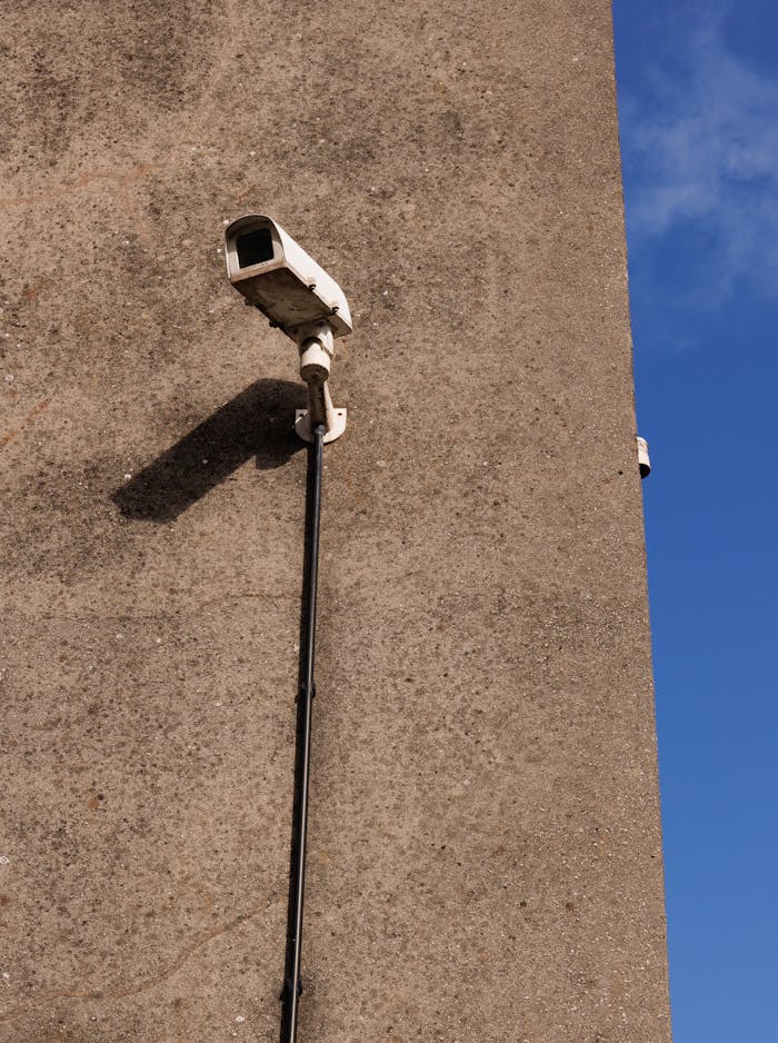 A security camera fixed on a concrete wall under a clear blue sky.