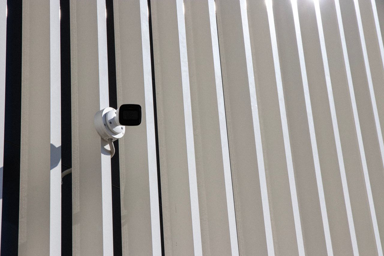 A security camera is mounted on a building with sleek, vertical lines creating a minimalist architectural effect.